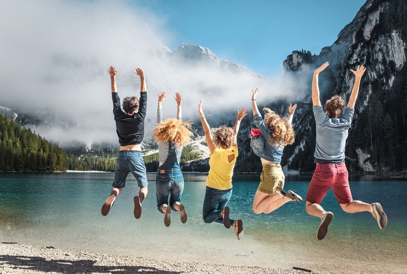 Mehr erleben – mit MiBon Die gleiche Gruppe junger Menschen springt in die Luft – mit Blick auf See und Berge. Lebensfreude pur, die mit MiBon zugänglich wird.