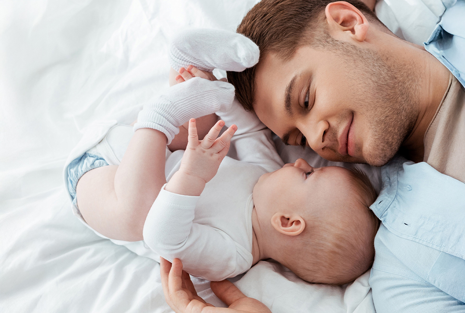 Unser Engagement Ein Vater liegt Gesicht an Gesicht mit seinem Kleinkind auf dem Bett – ein intimer Moment, der zeigt, wofür sich PRO LIFE einsetzt: Nähe, Familie, Menschlichkeit.