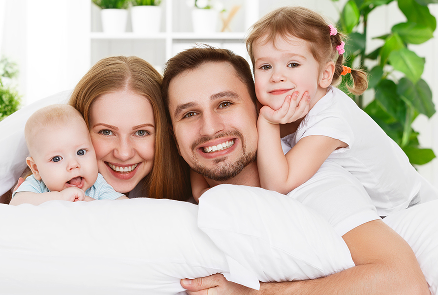 Familienfreundlich versichert Eine fröhliche Familie blickt über das Sofa direkt in die Kamera – für Ihre Anliegen rund um die Krankenkassenlösung.