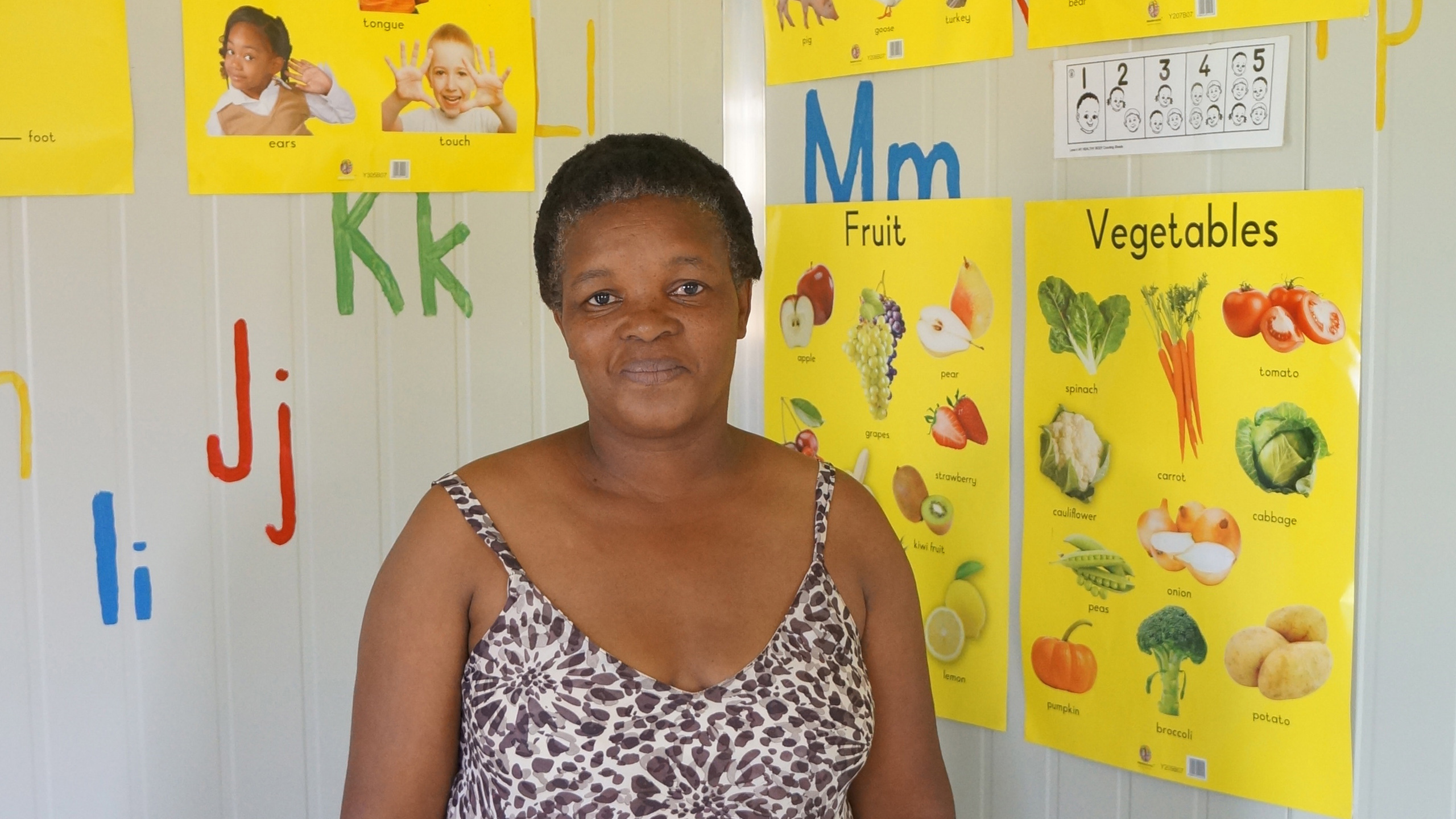 Lernen mit Begeisterung KITA-Leiterin Gladys vor bunten Unterrichtspostern – die Kinder sind begeistert vom neuen Schulalltag und kommen am liebsten täglich.