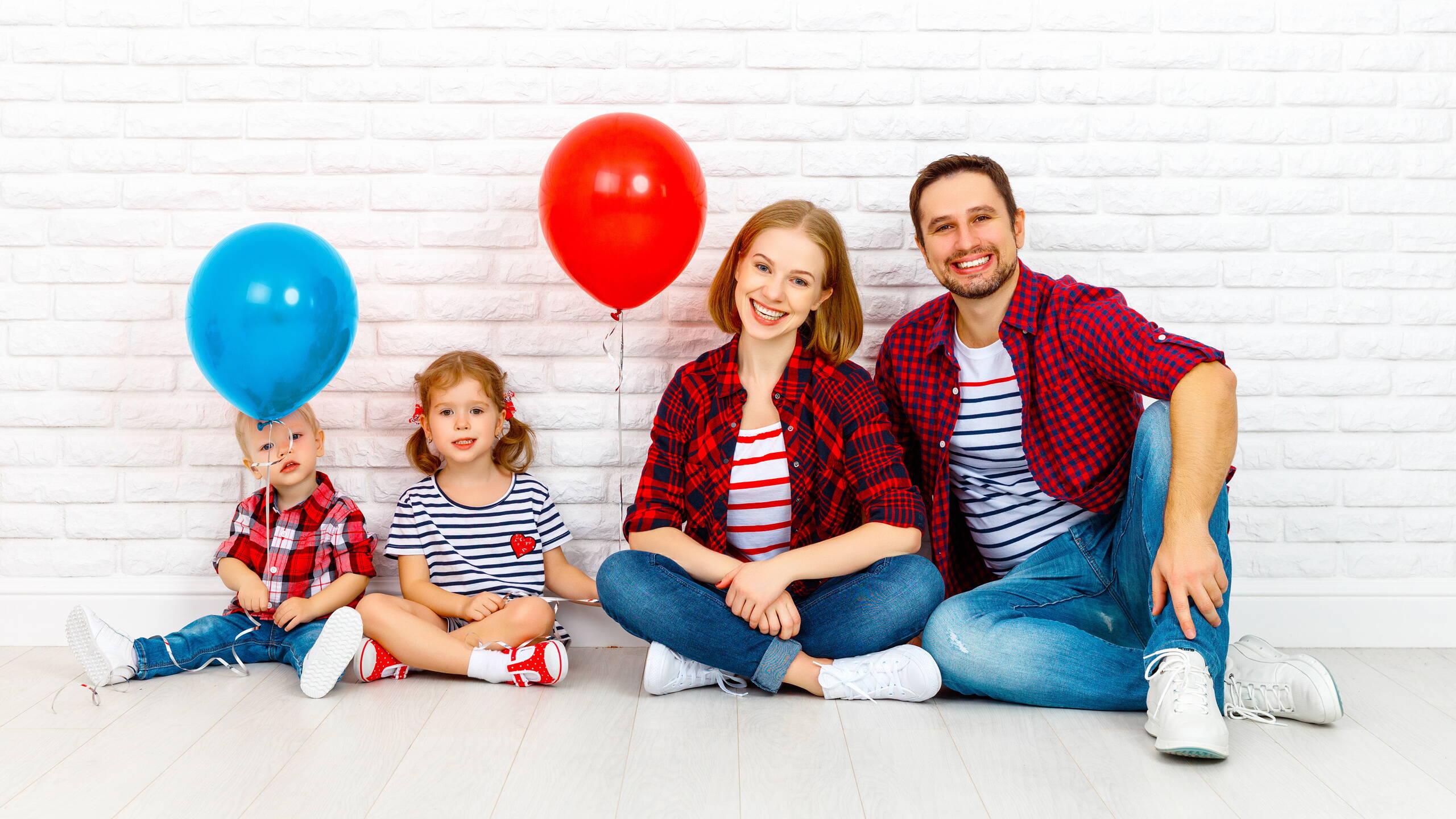 Mehr fürs Leben – mit PRO LIFE Eine vierköpfige Familie sitzt entspannt vor einer hellen Backsteinwand. Die Kinder halten bunte Ballone – ein Symbol für Leichtigkeit und Lebensfreude mit PRO LIFE.