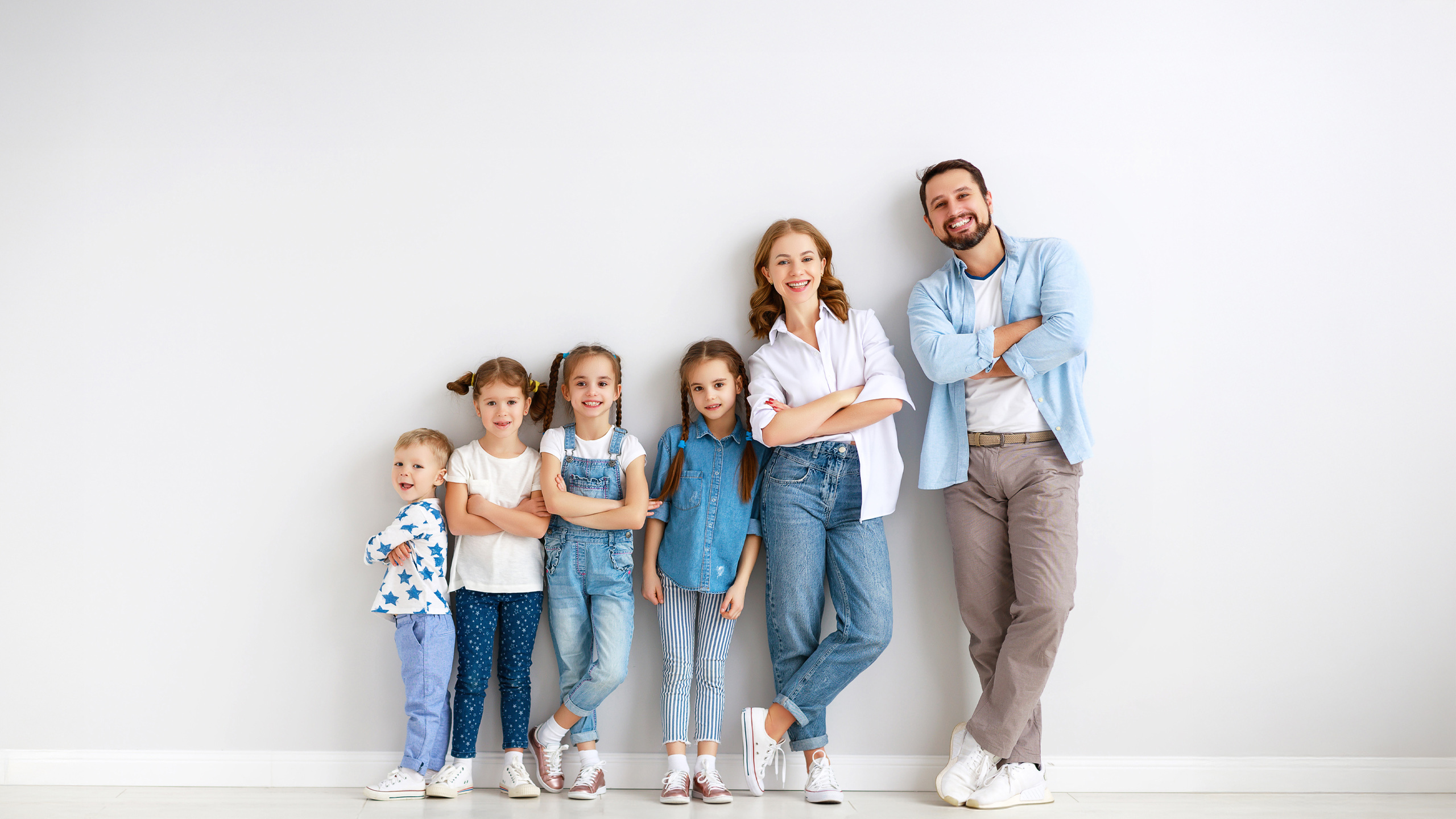 Gemeinsam für Ihre Familie Ein Elternpaar mit vier Kindern steht entspannt an eine graue Wand gelehnt – ein Bild für Zusammenhalt, Vertrauen und das, was wirklich zählt.