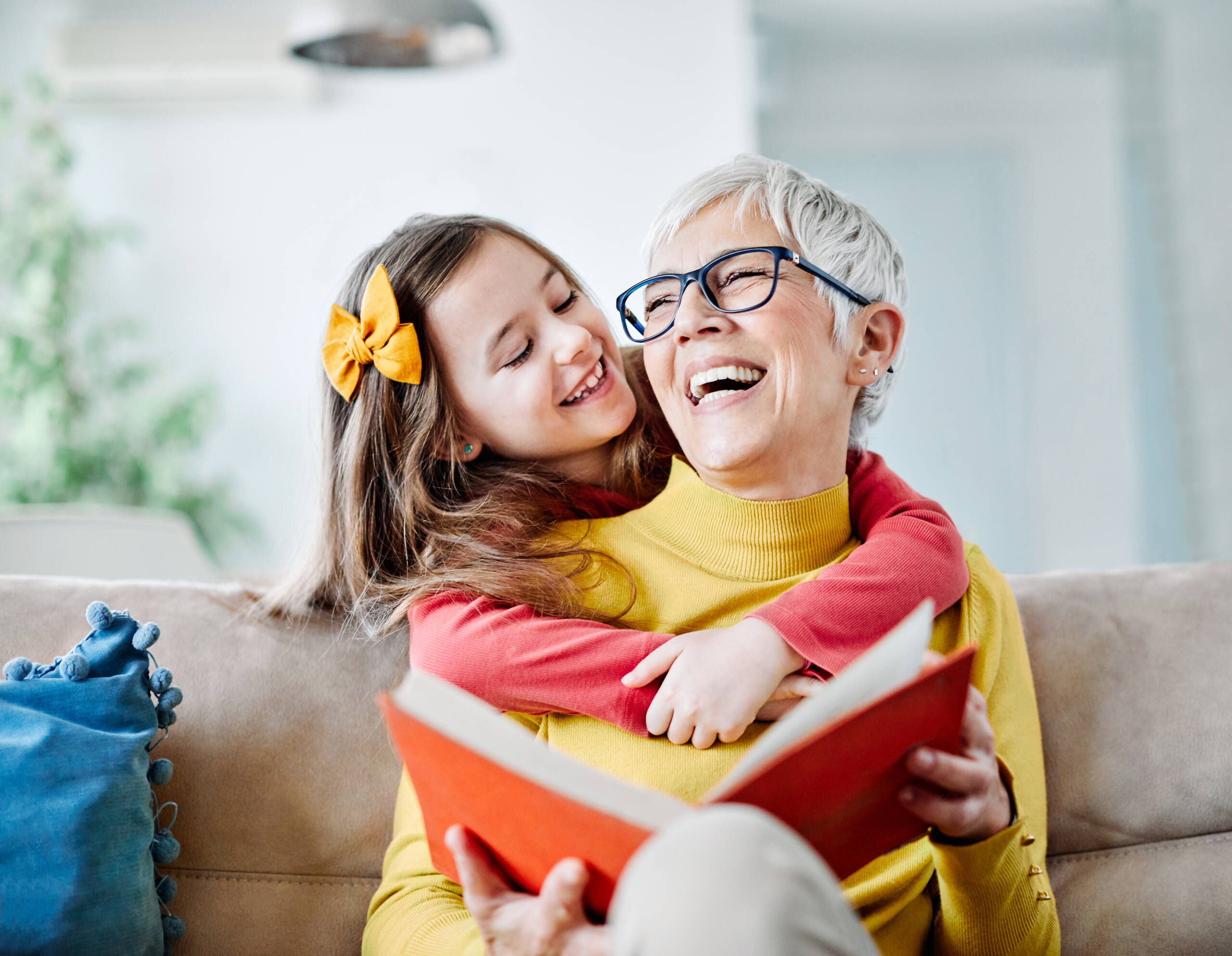 Alltagsunterstützung – Generationen im Miteinander Ein älterer Mensch sitzt mit einem Buch auf dem Sofa, begleitet von einer jüngeren Person. Das Bild steht für Fürsorge, zwischenmenschliche Nähe und praktische Hilfe im Alltag.