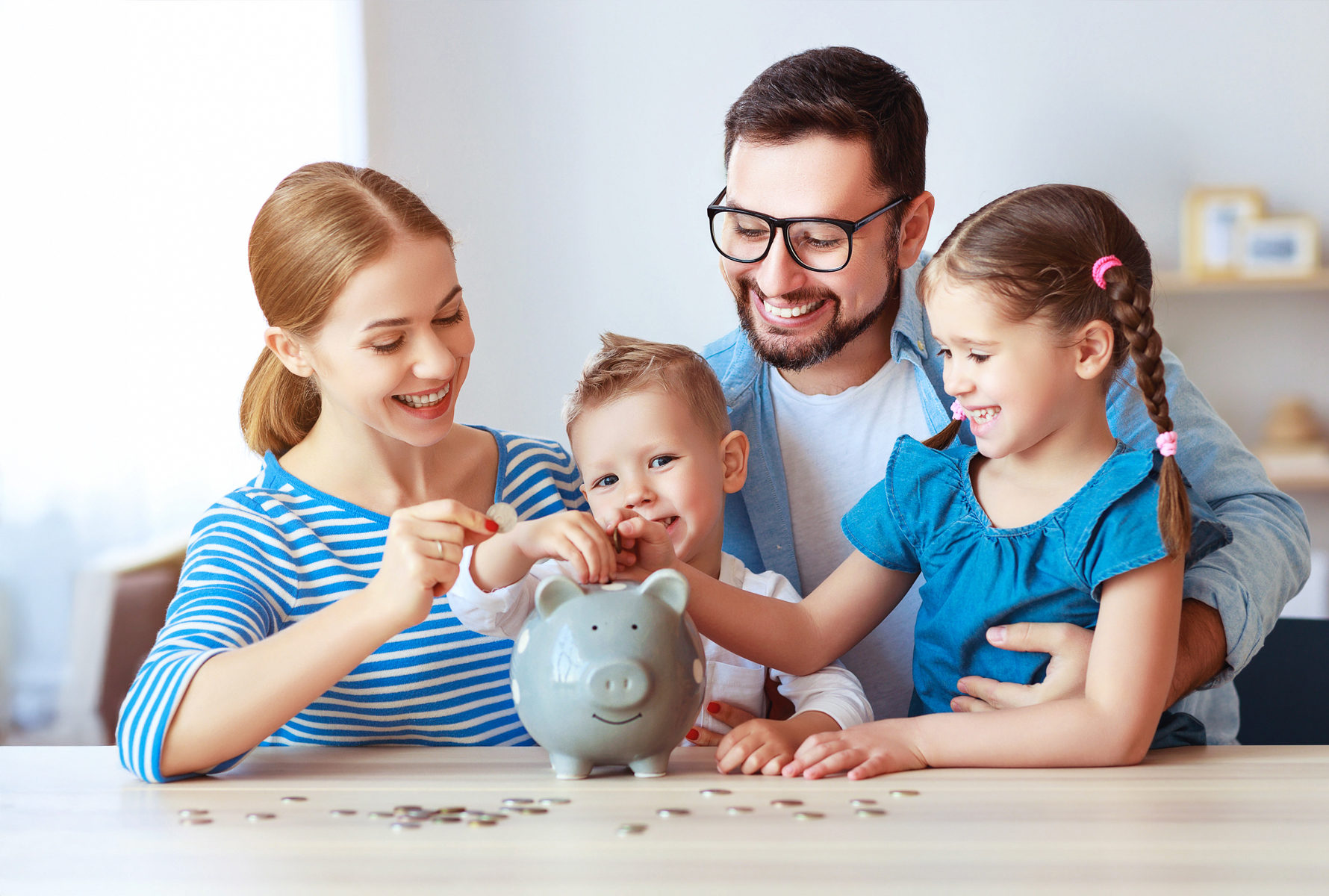 Sparen mit System Eine vierköpfige Familie sitzt am Tisch und füttert ein Sparschwein – so wirken sich die Vergünstigungen im Kollektivvertrag direkt auf Ihr Haushaltsbudget aus.