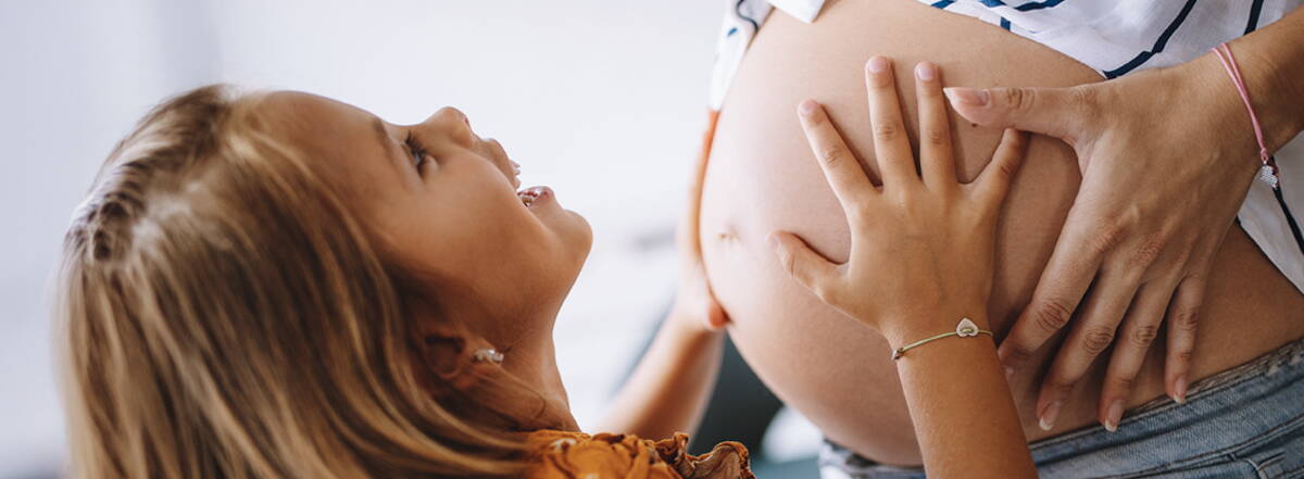 Schwangerschafts- & Babyblog Ein kleines Mädchen legt die Hände auf den Babybauch einer Schwangeren – ein liebevoller Blick in eine gemeinsame Zukunft.