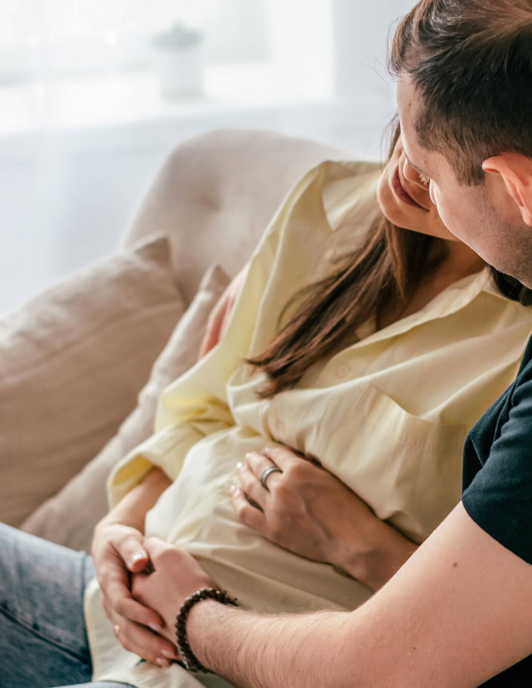 Paar versucht die Babybewegungen zu spüren Ein Paar sitzt entspannt auf dem Sofa, beide legen liebevoll die Hände auf den Bauch der Schwangeren – ein besonderer Moment der Verbundenheit.