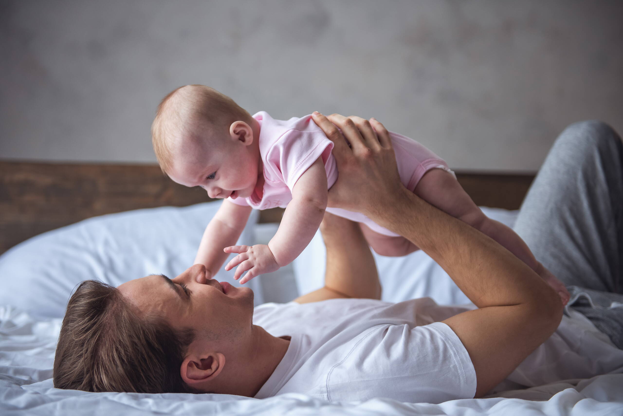 Padre e figlio in un momento di fiducia Un giovane padre è sdraiato sulla schiena, rilassato, e tiene teneramente il figlio sopra di sé – un’immagine di sicurezza e vicinanza.