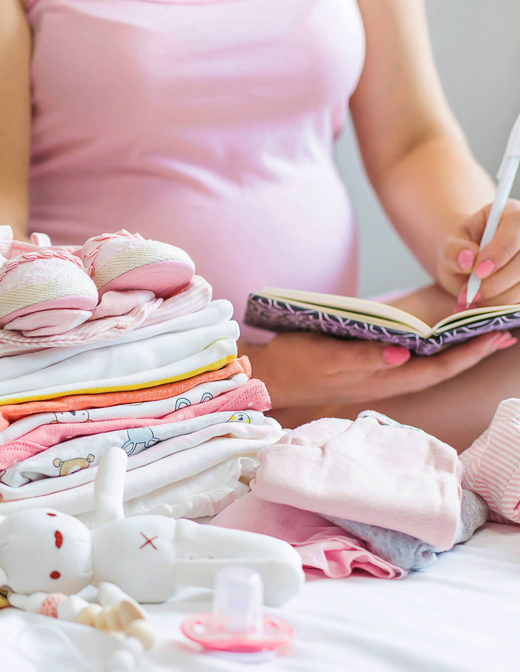 Momente für immer festhalten Eine schwangere Frau macht Notizen in ein Buch, im Vordergrund liegt liebevoll gefaltete Babykleidung – Erinnerungen für die Zukunft entstehen.