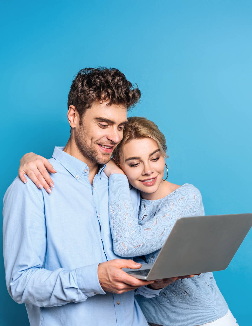 Leggere insieme gli articoli del blog L’immagine mostra due persone che guardano insieme un computer portatile. Entrambe indossano abiti azzurri e si trovano davanti a uno sfondo blu. Una persona tiene il computer portatile, mentre l’altra le cinge le spalle con il braccio.